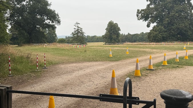 A black gate and yellow traffic cones leading to a field laid out as a car park